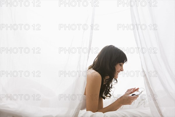 Caucasian woman laying in bed listening to mp3 player