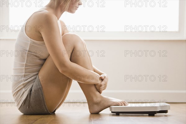 Caucasian woman sitting on floor near scale