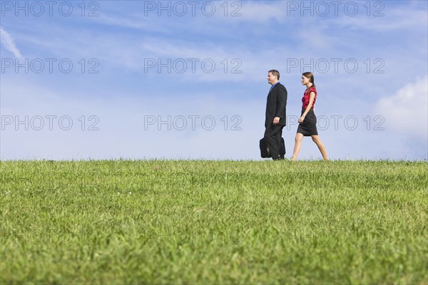 Caucasian co-workers walking through grassy field