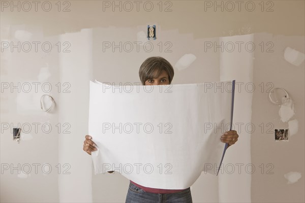 Mixed race woman standing in unfinished room with blueprints