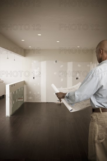 African American man standing in unfinished room with blueprints