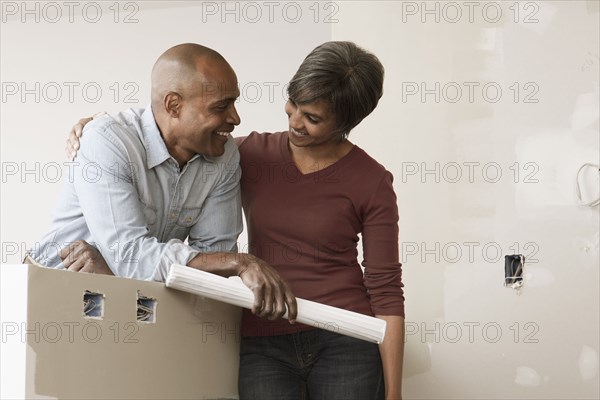 Couple standing in unfinished room with blueprints