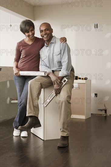 Couple with level and blueprints in unfinished room