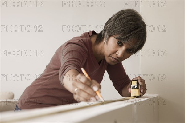 Mixed race woman measuring wall in unfinished room