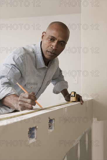 African American man measuring wall in unfinished room