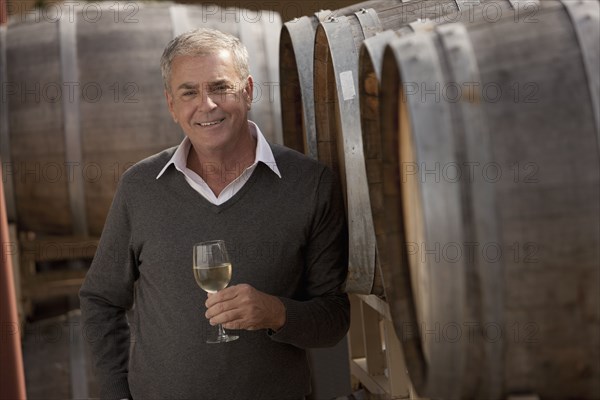 Caucasian man drinking wine near wine barrel