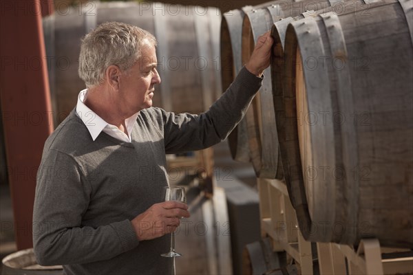 Caucasian man drinking wine near wine barrel