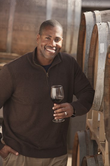 Black man drinking wine near wine barrel