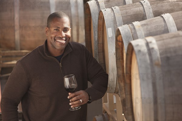 Black man drinking wine near wine barrel