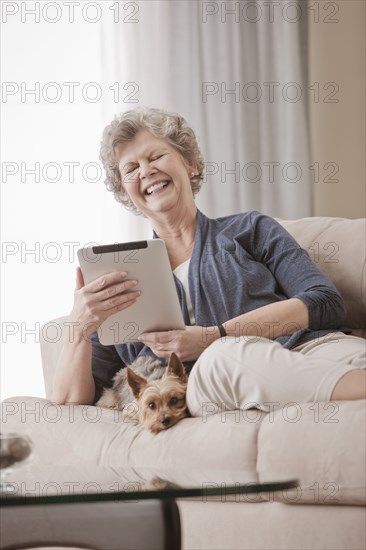 Caucasian woman sitting on sofa using digital tablet with dog