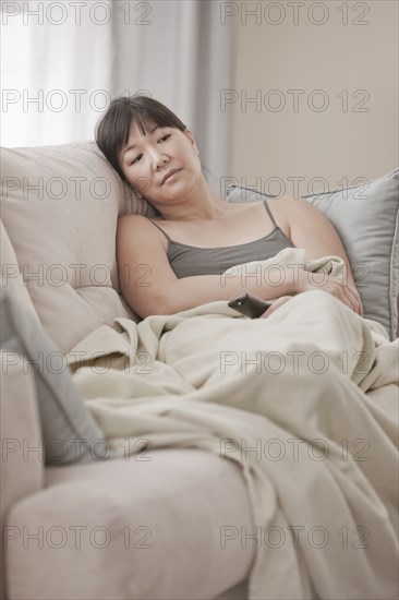 Asian woman laying on sofa watching television