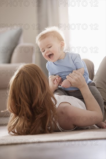Caucasian mother laying on floor playing with son