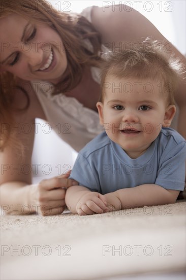 Caucasian mother laying on floor playing with son