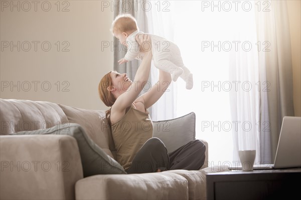 Caucasian mother on sofa lifting son