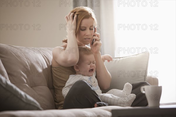 Caucasian mother holding crying son and talking on cell phone