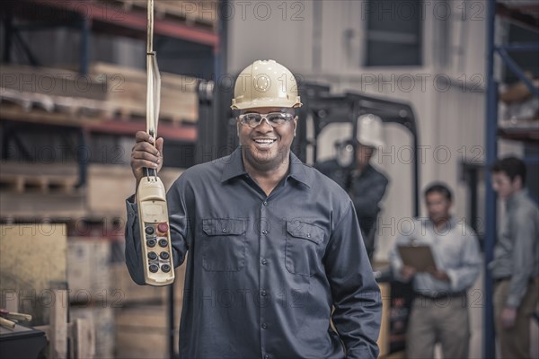 African American worker holding control panel in factory