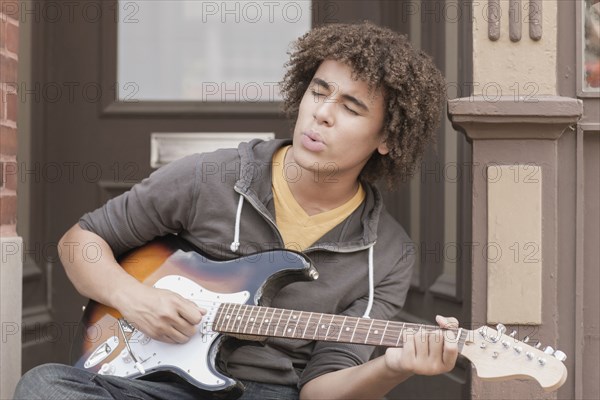 Mixed race teenager playing electric guitar and whistling
