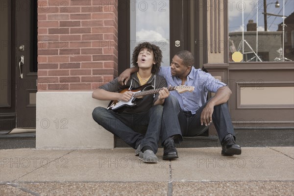 Father watching son playing electric guitar