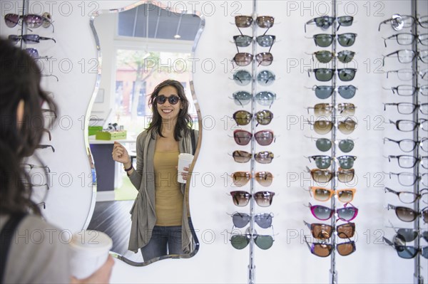 Mixed race woman drinking coffee and looking at eyeglasses in shop