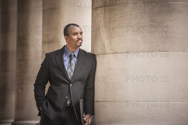 Mixed race businessman leaning on column