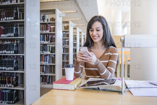 Student using cell phone at desk in library