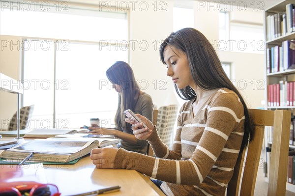 Student using cell phone at desk in library