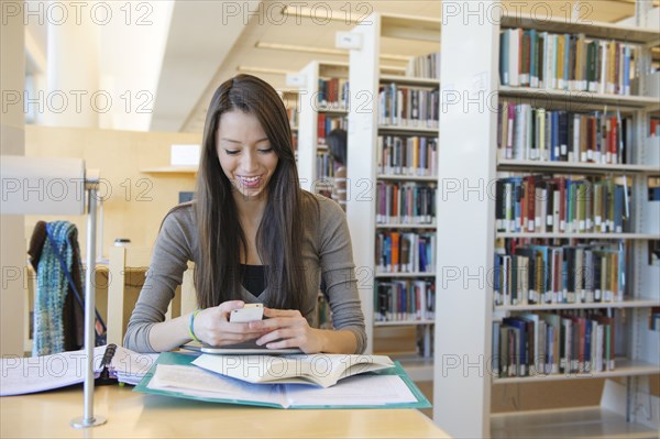 Student using cell phone at desk in library