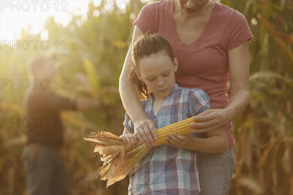 Caucasian mother and daughter examining ear of corn