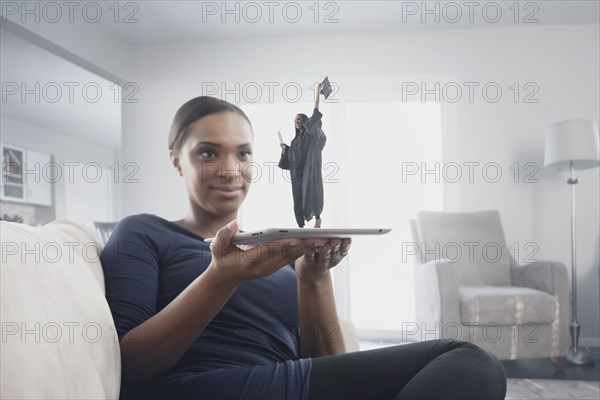 Black woman watching figure of graduate standing on digital tablet