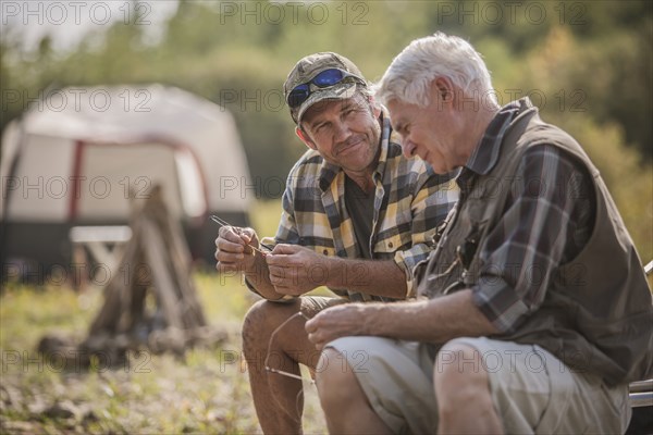 Caucasian father and son tying fishing lures at campsite