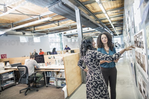 Businesswomen examining photographs on wall in office