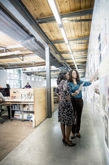 Businesswomen examining photographs on wall in office