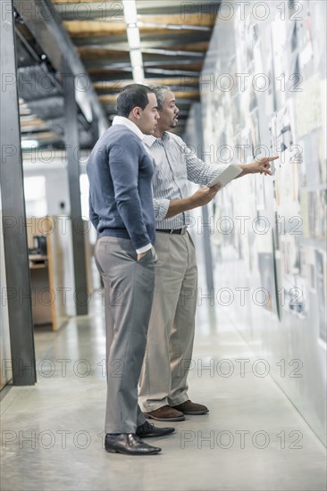 Businessmen examining photographs on wall in office