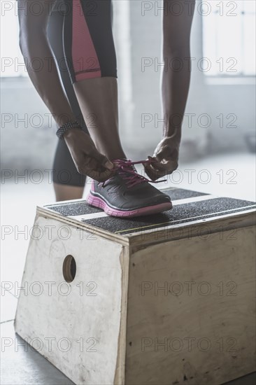 Athlete tying her shoes on platform in gym