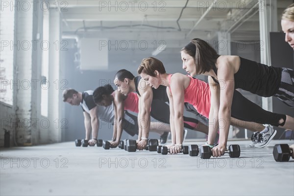 Athletes doing push-ups with dumbbells on floor