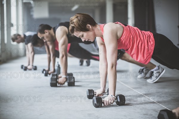 Athletes doing push-ups with dumbbells on floor