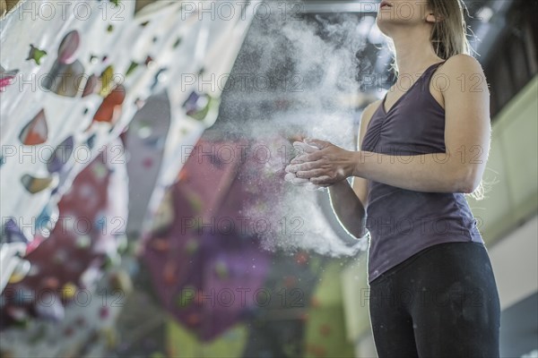 Athlete chalking her hands at rock wall in gym