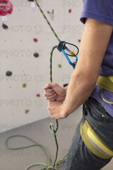 Athlete tying climbing harness at rock wall in gym