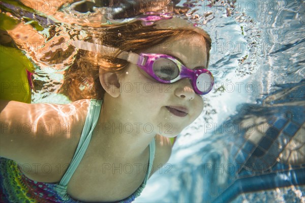 Caucasian girl swimming underwater in swimming pool