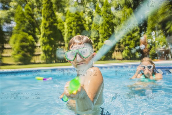 Caucasian boy playing with squirt gun in swimming pool