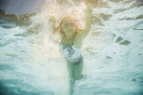 Caucasian girl swimming underwater in swimming pool