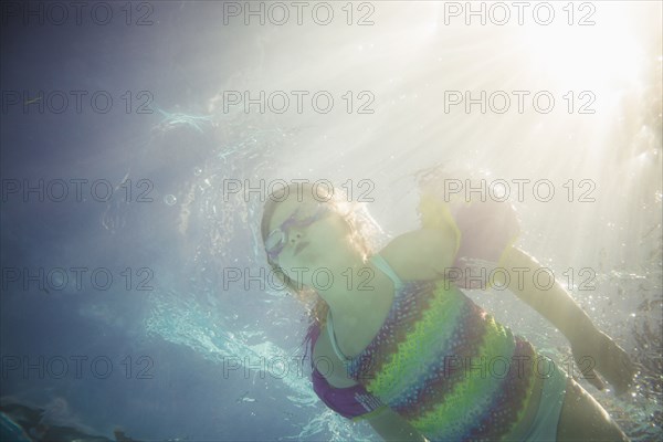 Caucasian girl swimming underwater in swimming pool