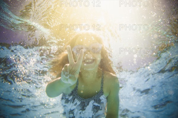 Caucasian girl swimming underwater gesturing peace sign