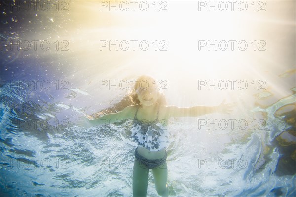 Caucasian girl swimming underwater in swimming pool