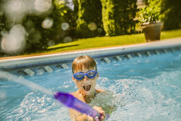 Caucasian boy playing with squirt gun in swimming pool