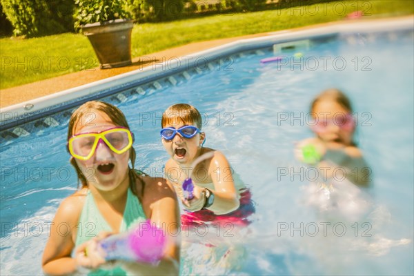 Caucasian children playing with squirt guns in swimming pool