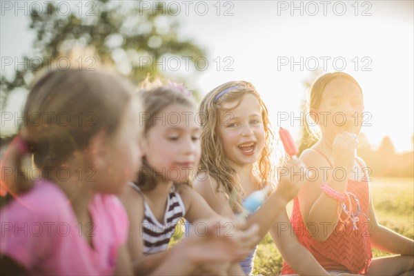 Girls eating flavored ice in sunny field