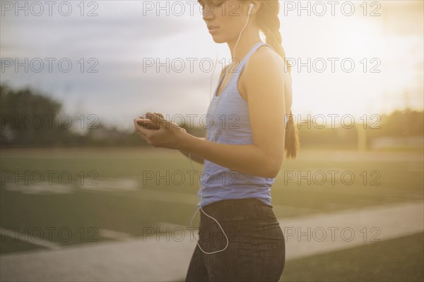 Mixed race athlete listening to mp3 player on sports field