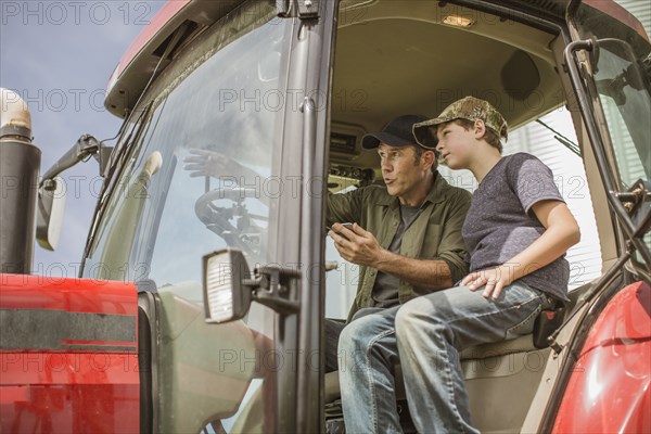 Caucasian farmer teaching son to drive tractor