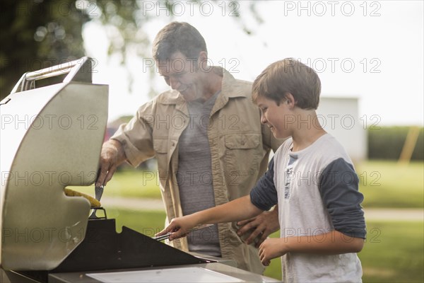 Caucasian father and son grilling food in backyard